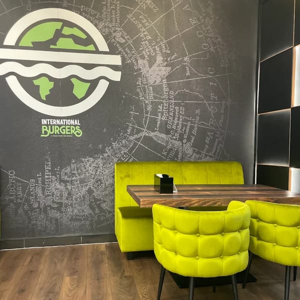 International Burgers restaurant interior with lime green seating, wooden tables, and a world map mural.