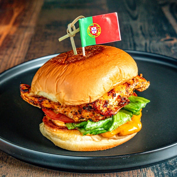 A Portuguese chicken burger with lettuce, tomato, and sauce on a black plate.