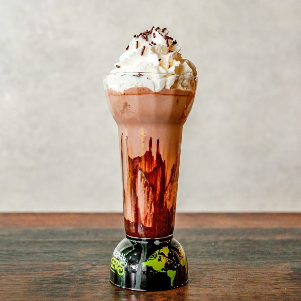 International Burgers' chocolate milkshake with whipped cream, chocolate drizzle, and sprinkles in a branded glass.