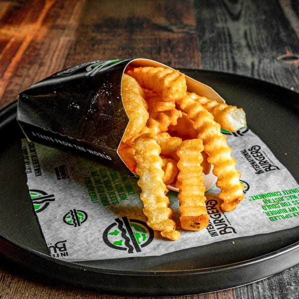 Crispy crinkle-cut fries in an International Burgers branded paper cone on a dark plate.