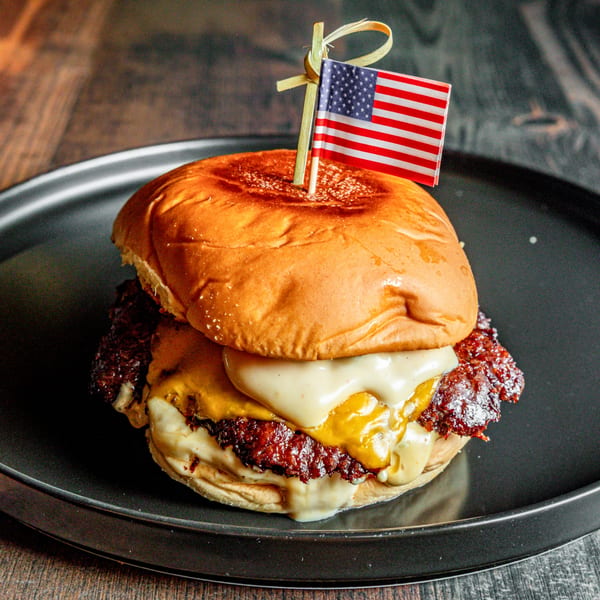 A cheesy International Burgers' burger with a small American flag on a black plate.