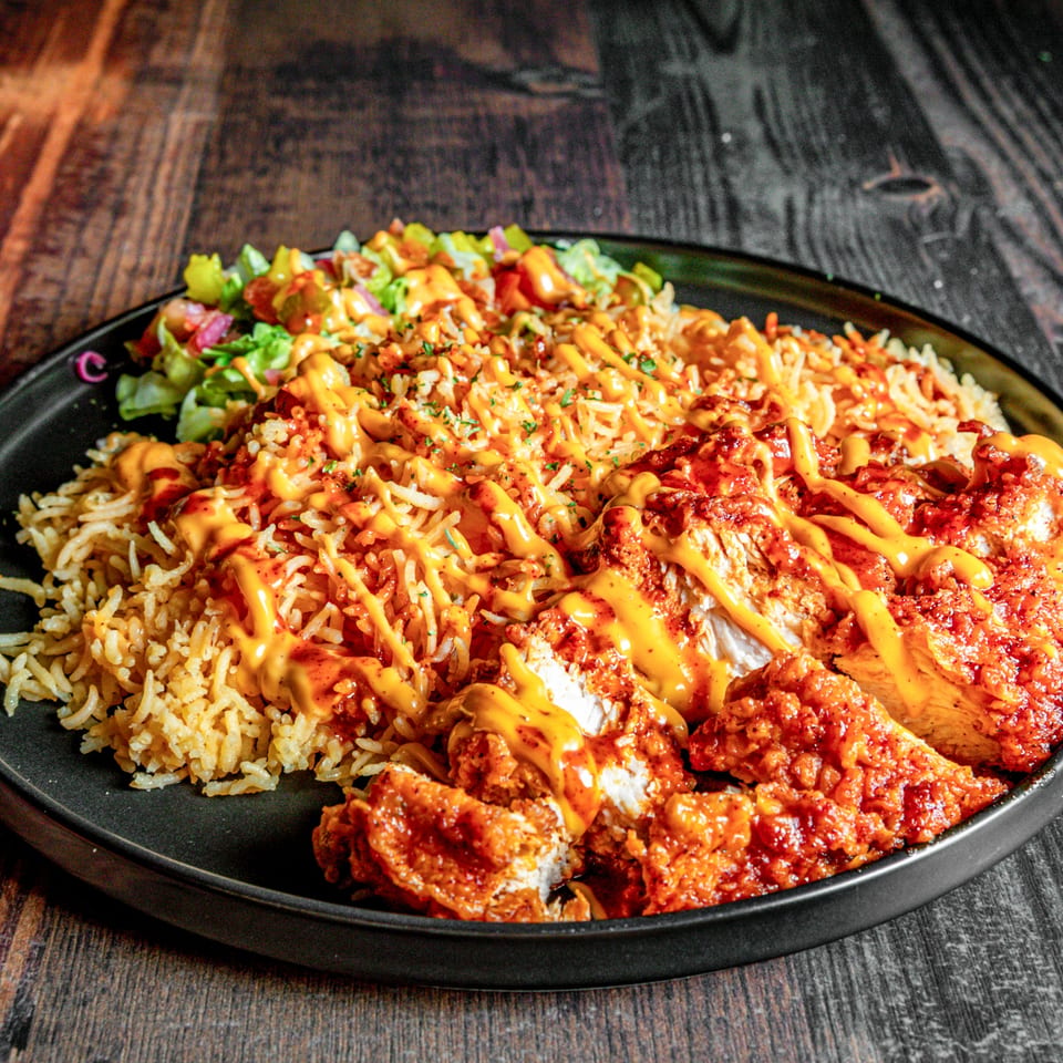 Spicy fried chicken pieces, rice, and a side salad drizzled with sauce on a dark plate.