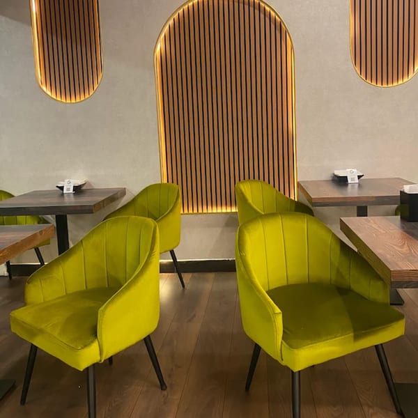 Modern restaurant interior with bright lime green chairs, dark wood tables, and illuminated slatted wall decor.