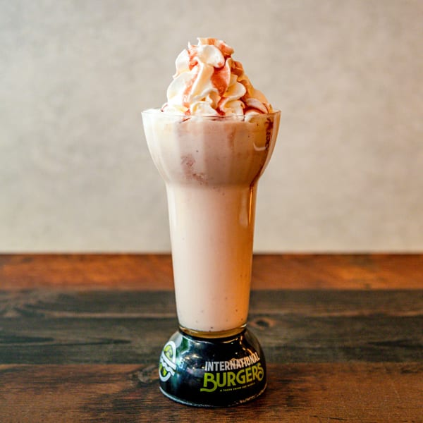 Milkshake with whipped cream and caramel drizzle in an International Burgers branded glass.