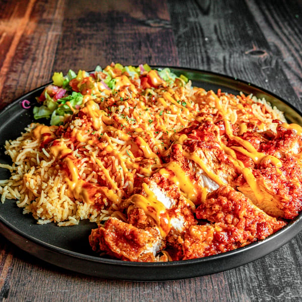 Spicy fried chicken pieces with rice and a side salad, drizzled with orange sauce.