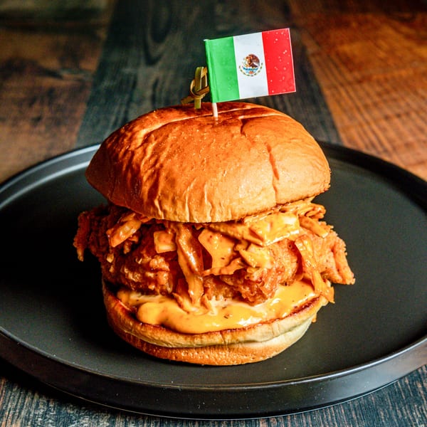 A Mexican-themed burger with a flag on top, served on a dark plate.